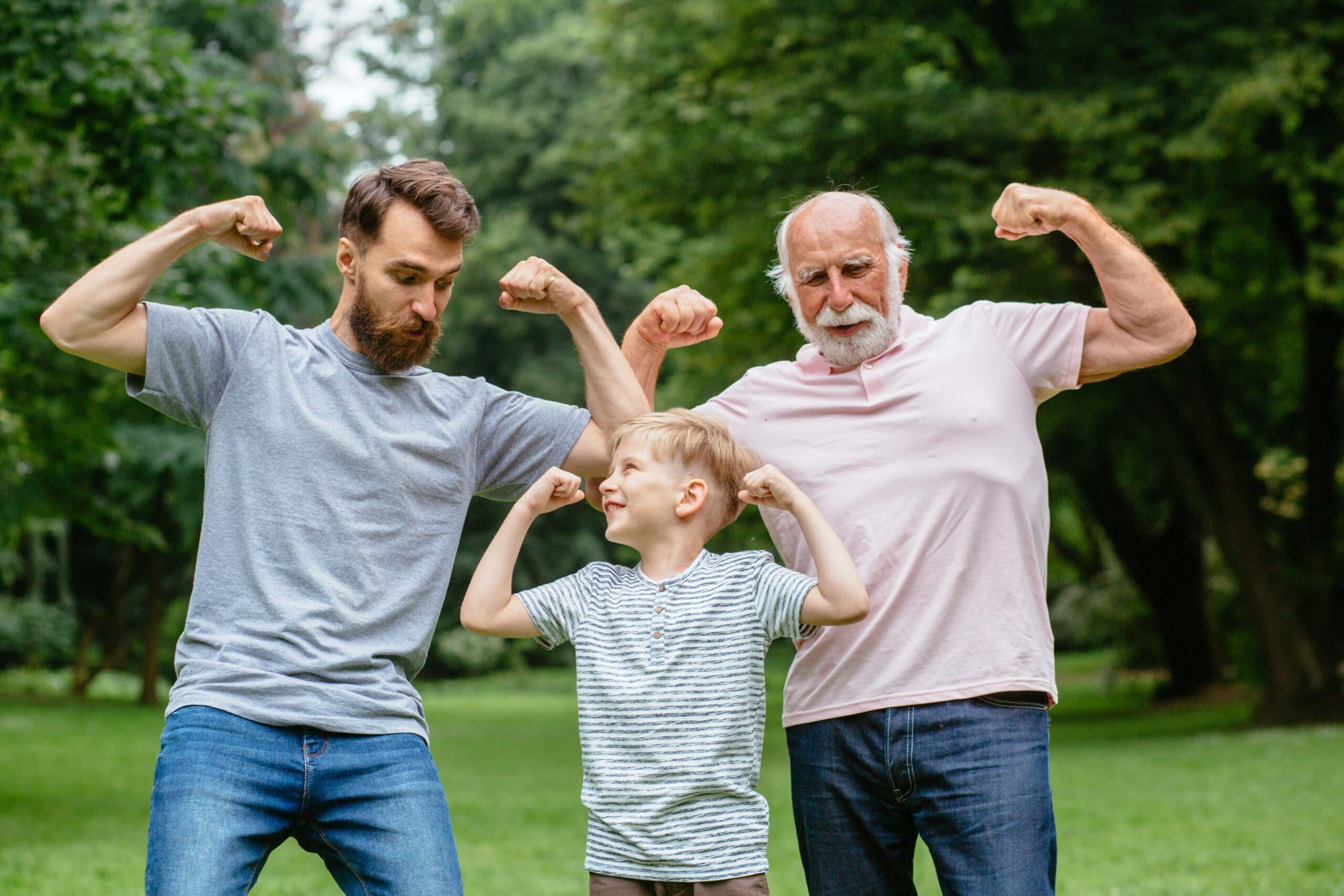 Men's health: A grandpa, father and his son smiling and showing their muscles outdoor in park on background. Three different generation concept.